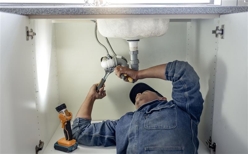 Plumber repairing pipes beneath a bathroom sink in Loveland