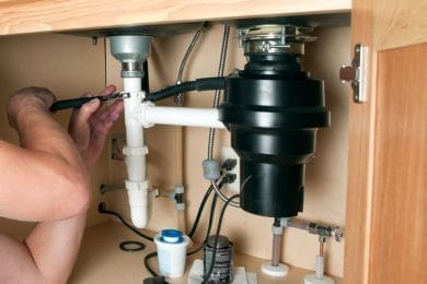 Plumber repairing a garbage disposal beneath a kitchen sink in Loveland