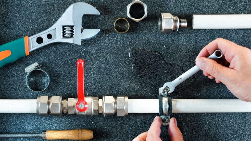 Plumber repairing a pipe valve with an adjustable wrench in Loveland