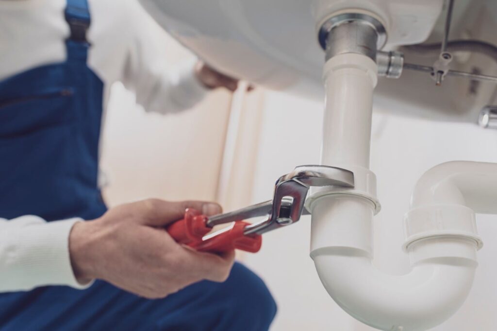 Plumber repairing a white drain pipe beneath a sink in Loveland