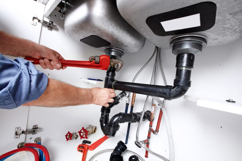 Plumber repairing drain pipes beneath a kitchen sink in Loveland
